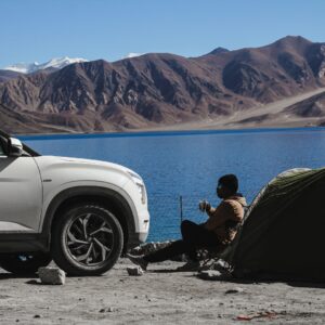 man in black jacket sitting on black camping chair near white car during daytime