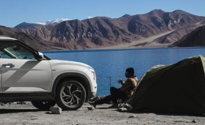 man in black jacket sitting on black camping chair near white car during daytime