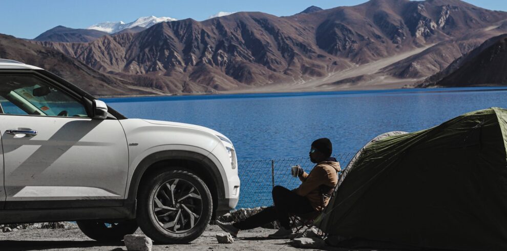 man in black jacket sitting on black camping chair near white car during daytime